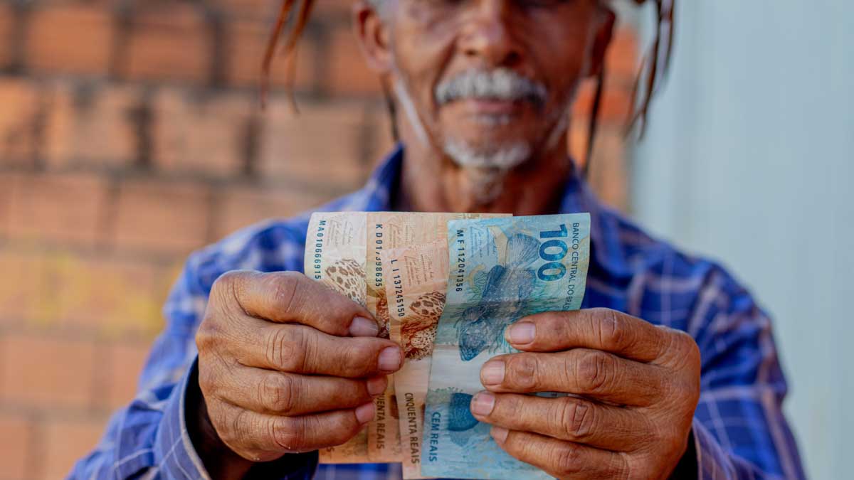 aposentado segurando notas de 100 e 50 do empréstimo consignado
