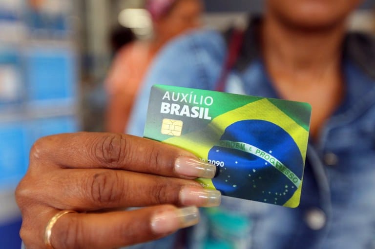 Mulher negra segurando um cartão do auxílio Brasil.