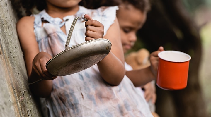 Uma menina segurando um prato de alumínio e um menino segurando uma caneca laranja.