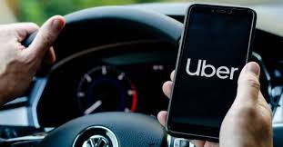 motorista de aplicativo com mão no volante e celular com aplicativo do uber aberto na tela