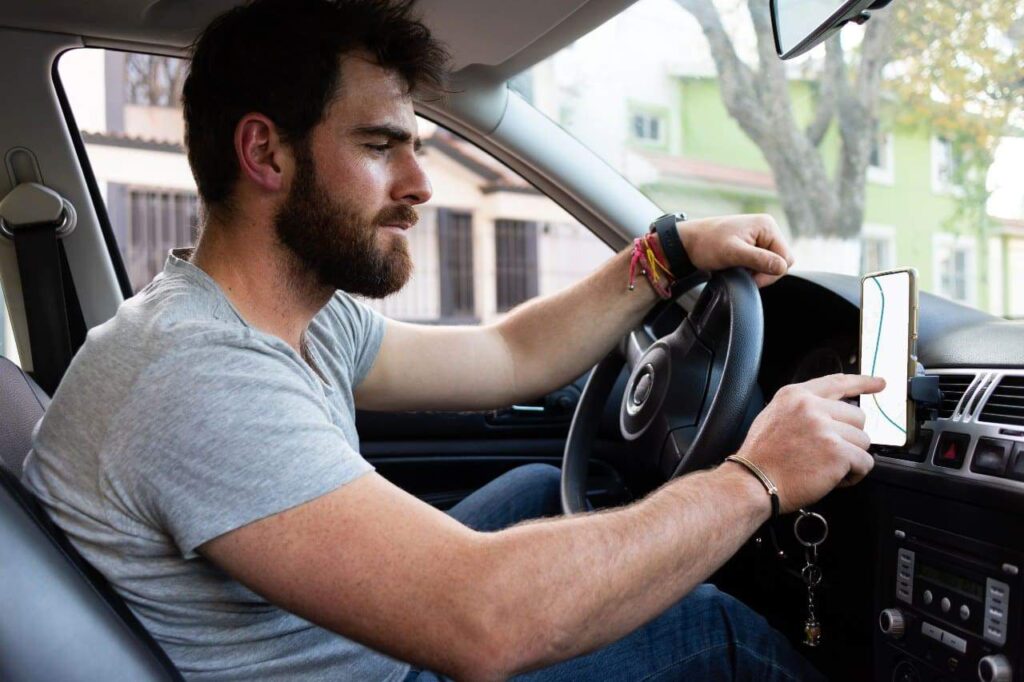 Motorista de aplicativo dentro do carro buscando o destino do seu passageiro no celular