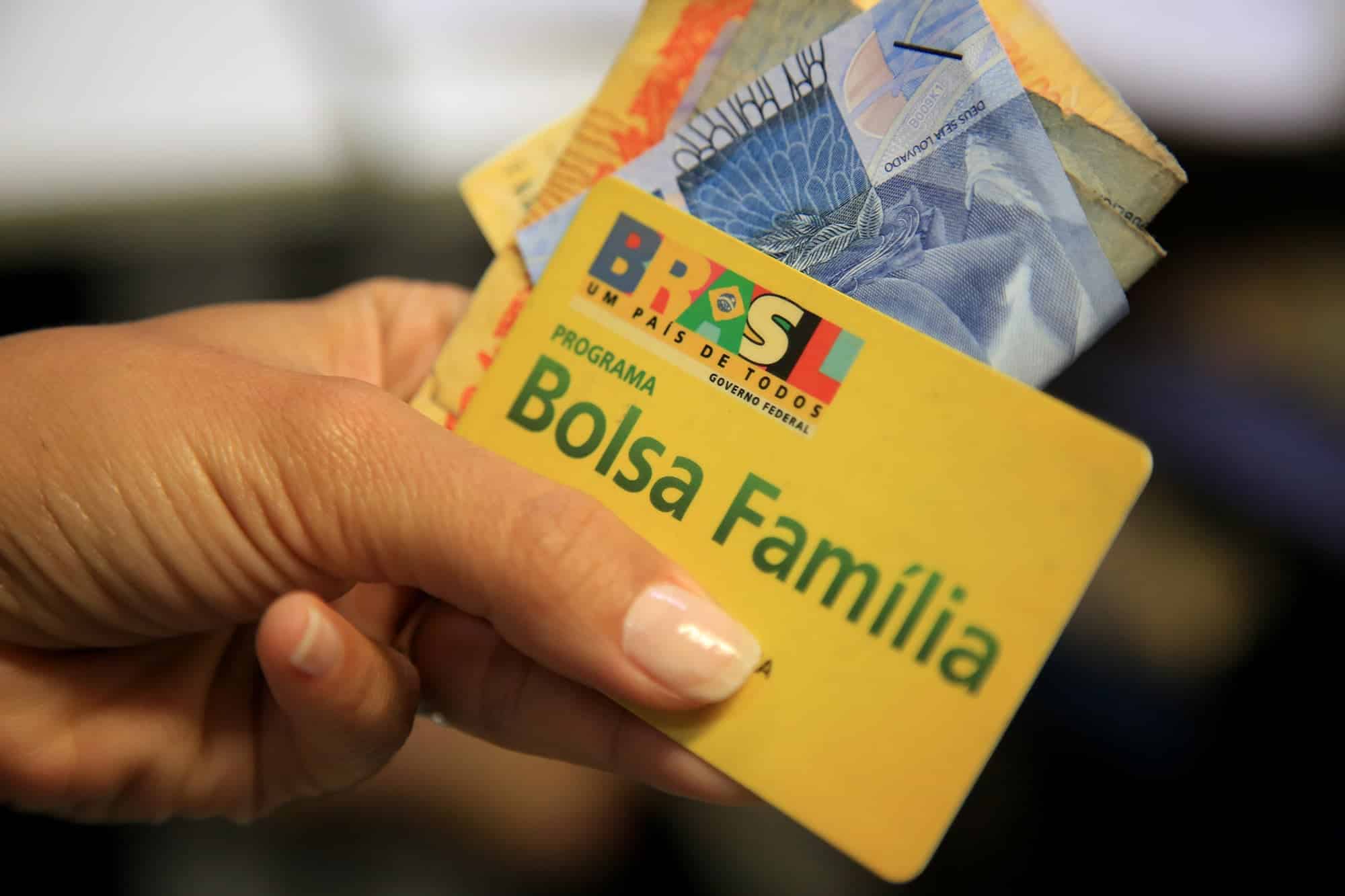 imagem com mão segurando dinheiro e o cartão do benefício para ilustrar o pagamento do Bolsa Família antecipado