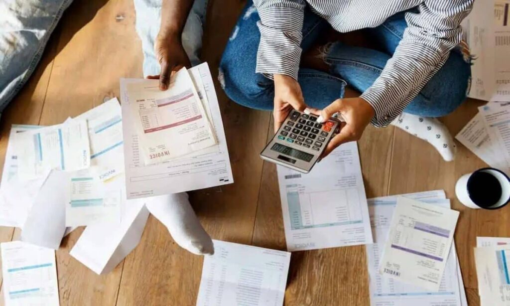 pessoa com diversas contas ao seu redor e uma calculadora