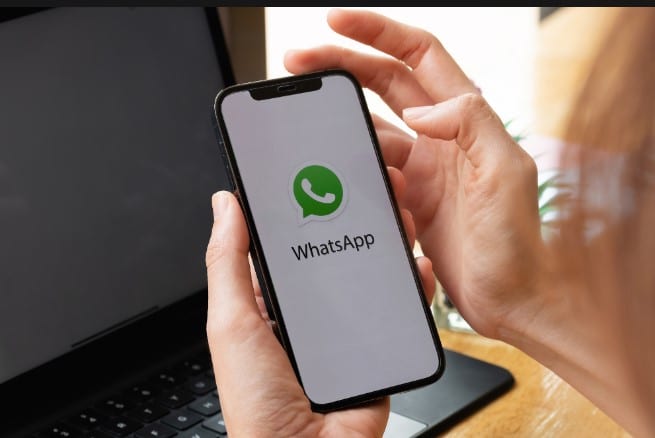 Imagem de mãos segurando um celular com o WhatsApp aberto na tela