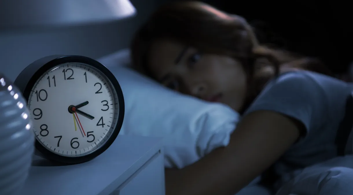 mulher tentando dormir na cama ao lado do despertador
