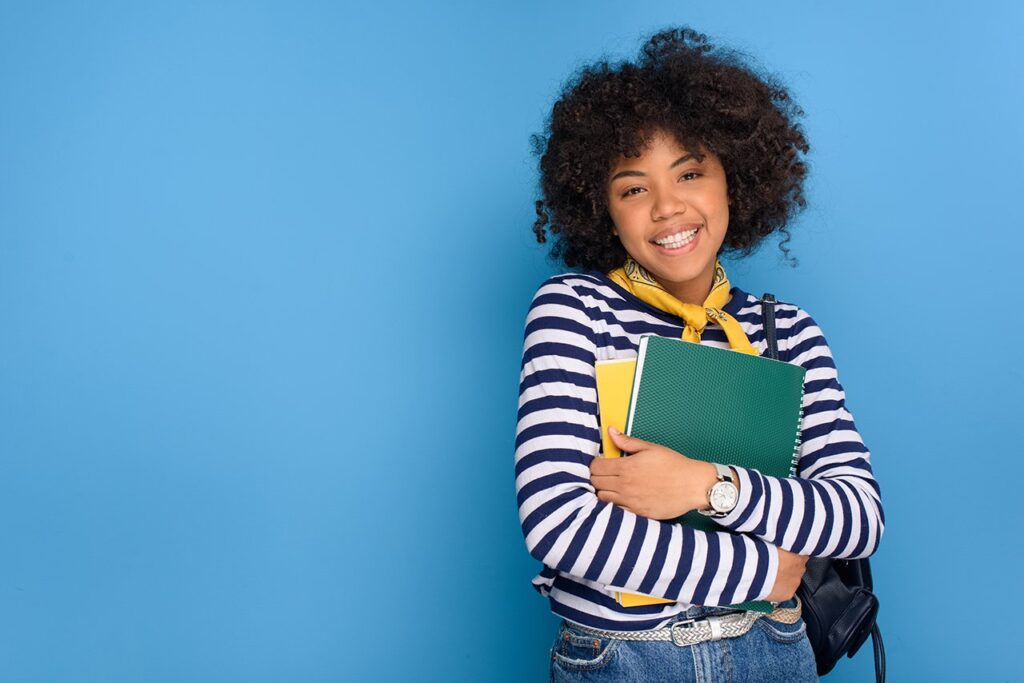 jovem negra sorrindo segurando cadernos