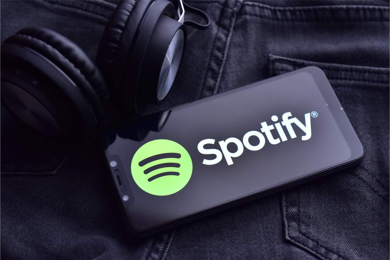 celular com a tela do spotify em cima de uma calça jeans com um fone de ouvido