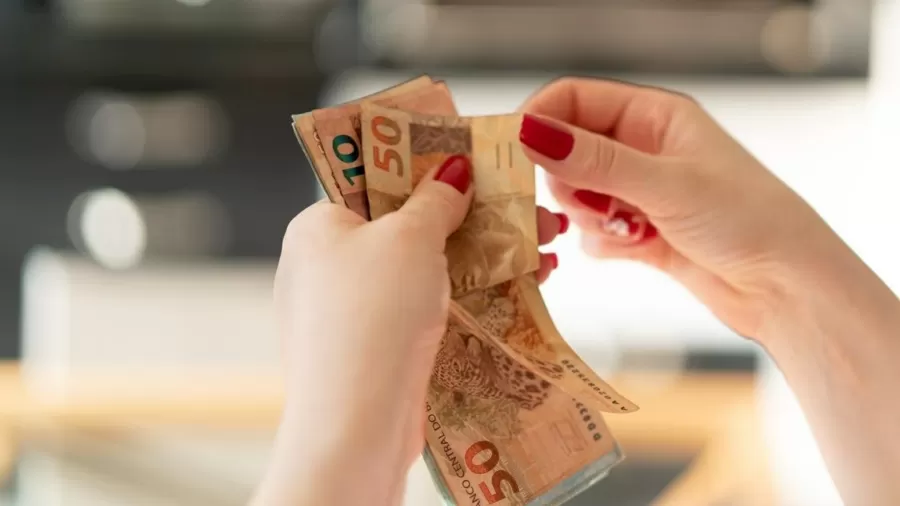 mão feminina segurando cédulas de 50 e 10 reais