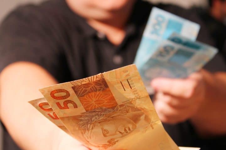 mulher segurando cédulas de 50 e 100 reais