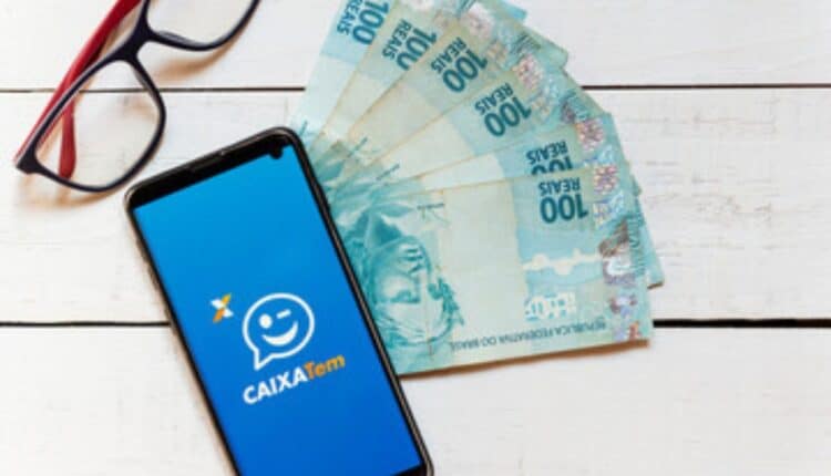 celular aberto no caixa tem ao lado de cédulas de 100 reais