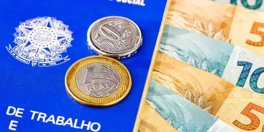 carteira de trabalho ao lado de notas de 100 e 50 reais