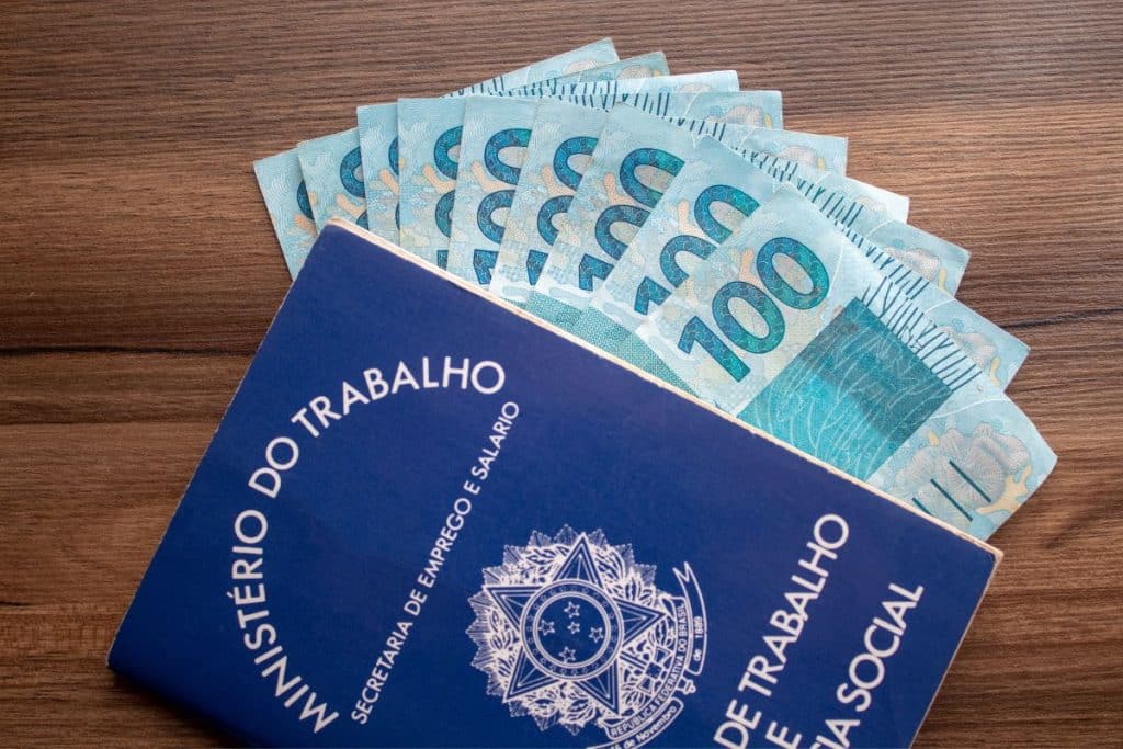 carteira de trabalho ao lado de cédulas de 100 reais